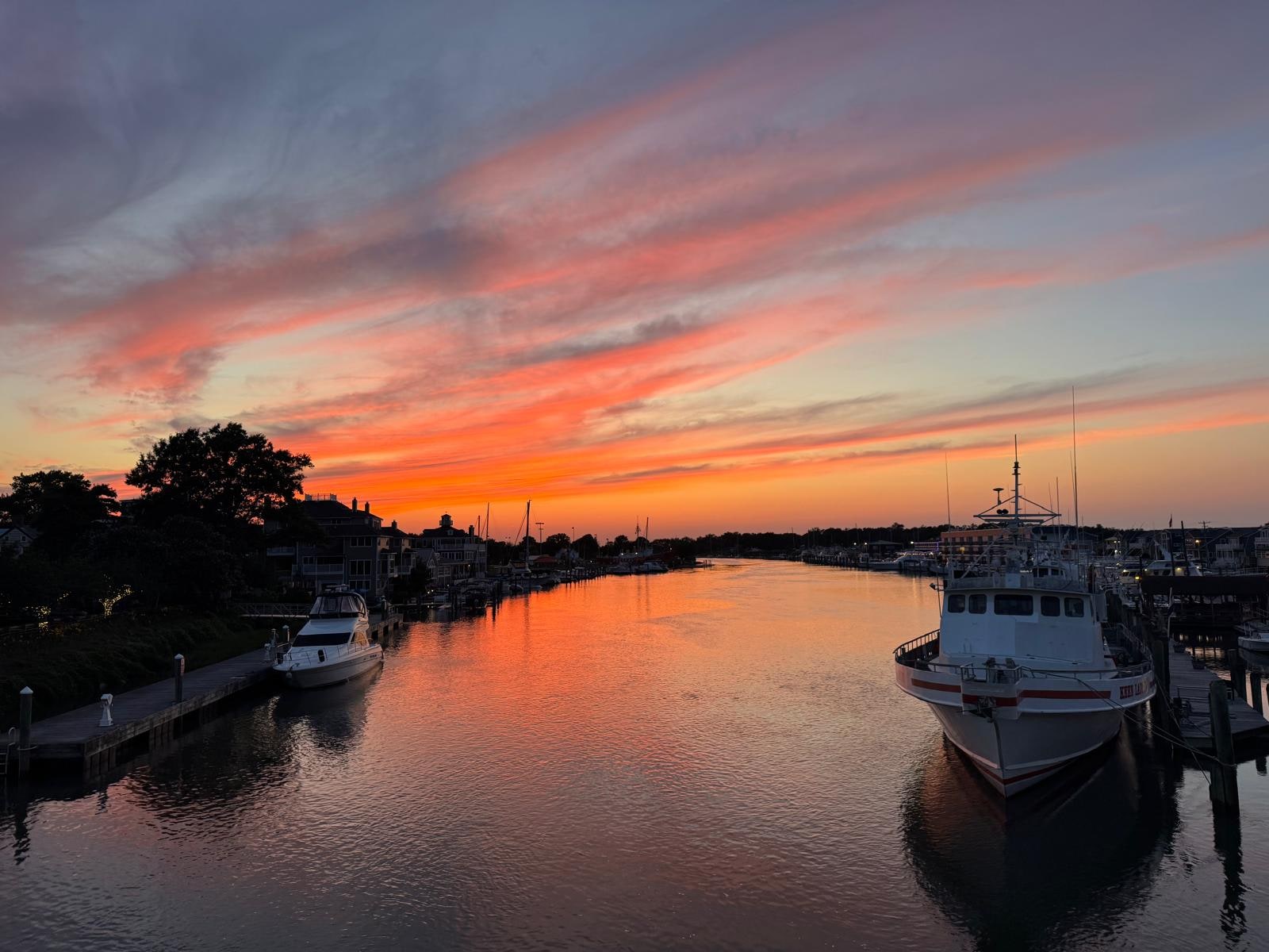 A coral sunset reflected across a marina with boats along both banks